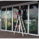 A man on a ladder painting the windows of a building.